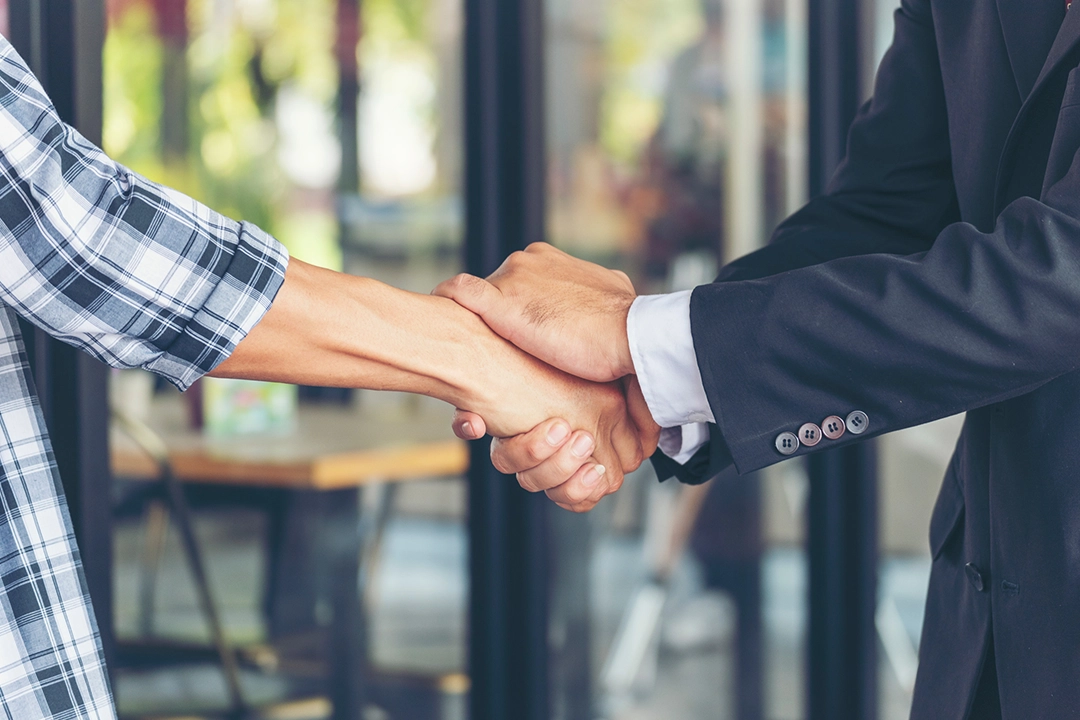 A close-up of a firm handshake between a person in a casual plaid shirt and a professional in a dark suit, symbolizing a deal or agreement