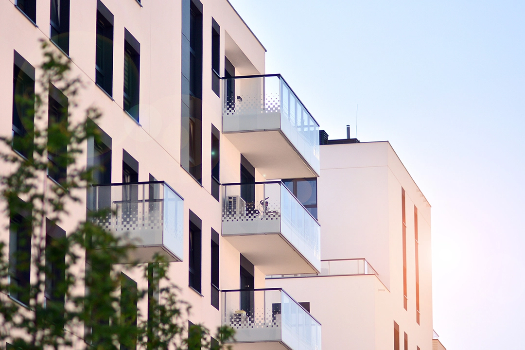 Exterior view of a modern, white apartment building with glass-railed balconies under a clear sky.