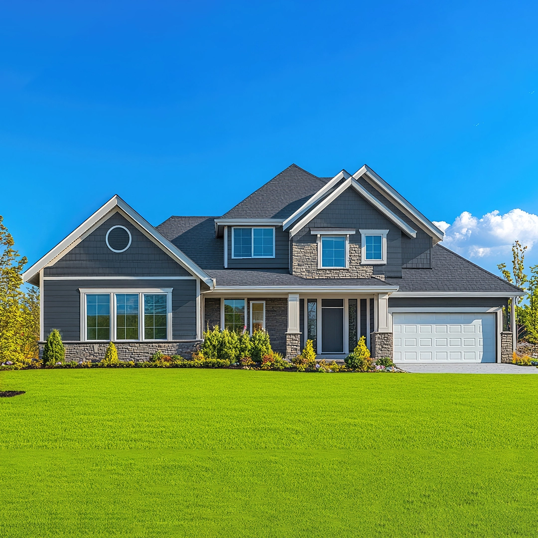 A modern gray house with stone accents, large windows, and a manicured lawn under a clear blue sky.